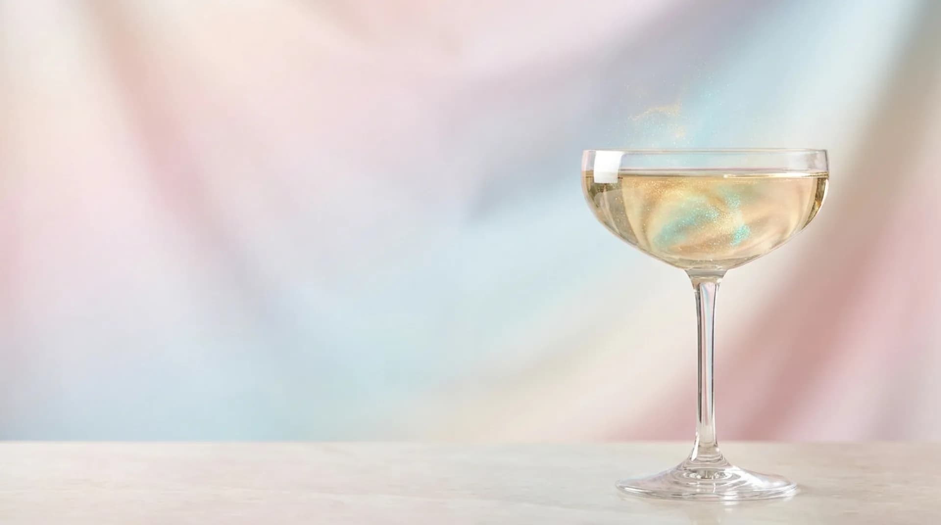 Une coupe de boisson pétillante et irisée sur un plan de marbre, fond nacré